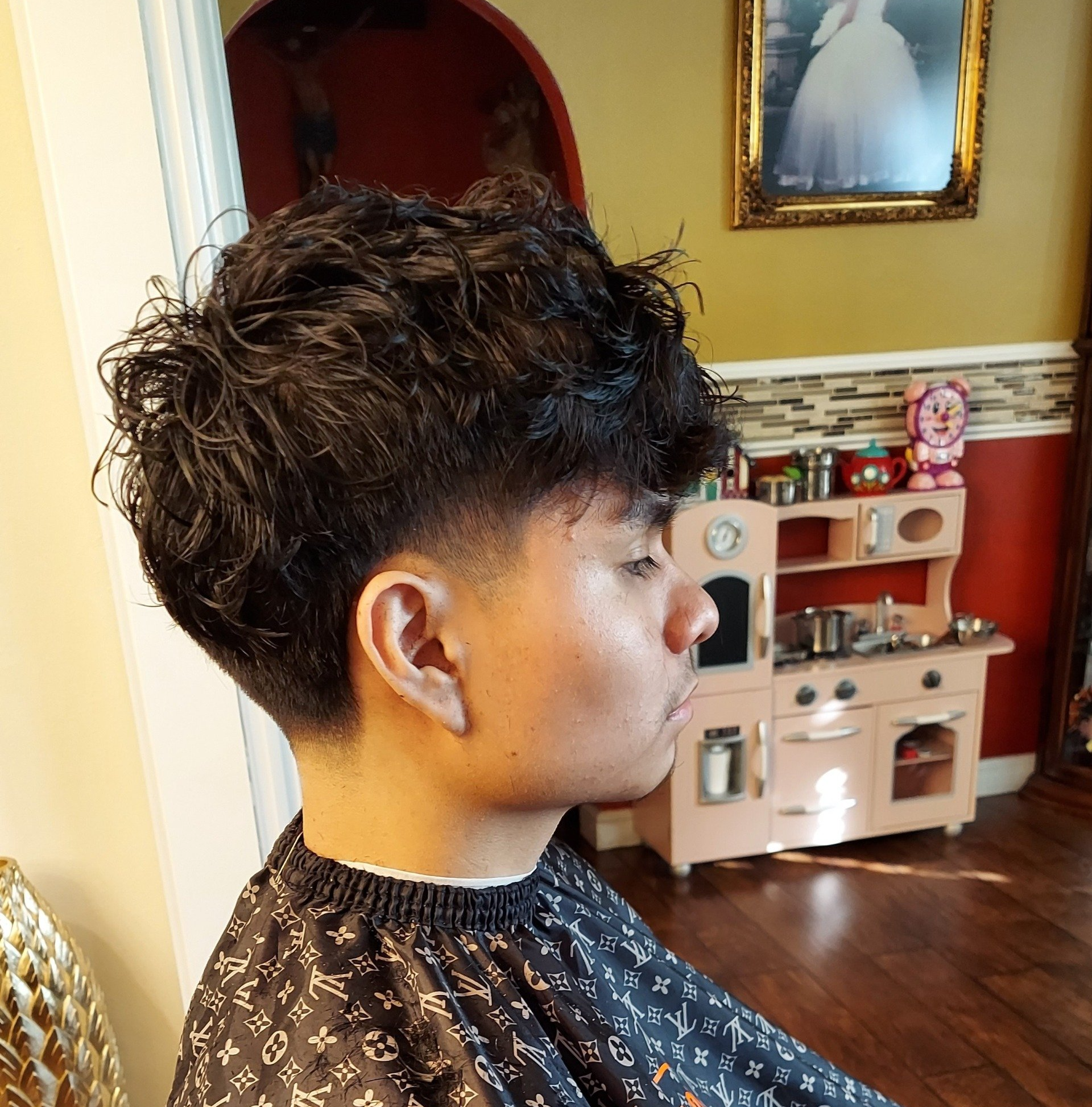 A man with curly hair is sitting in front of a play kitchen