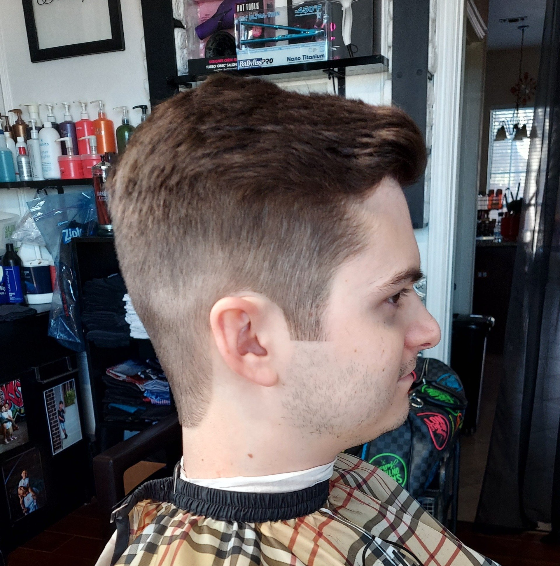 A man in a plaid cape is getting his hair cut