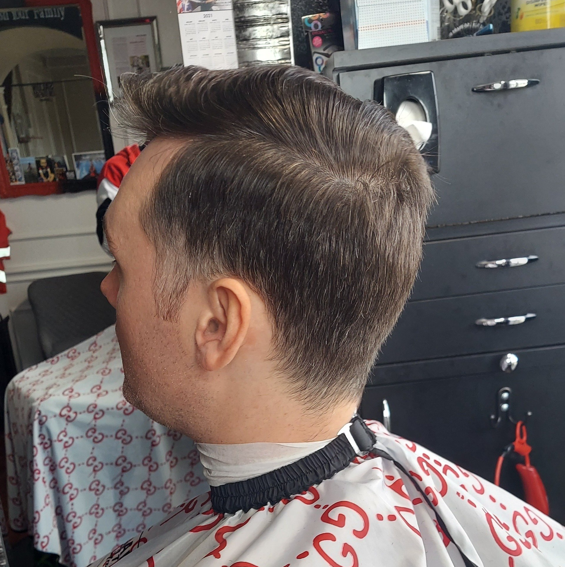 A man in a gucci cape is getting his hair cut