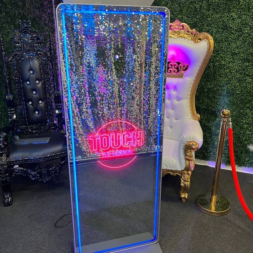 A mirror with a neon sign on it is sitting next to a chair.