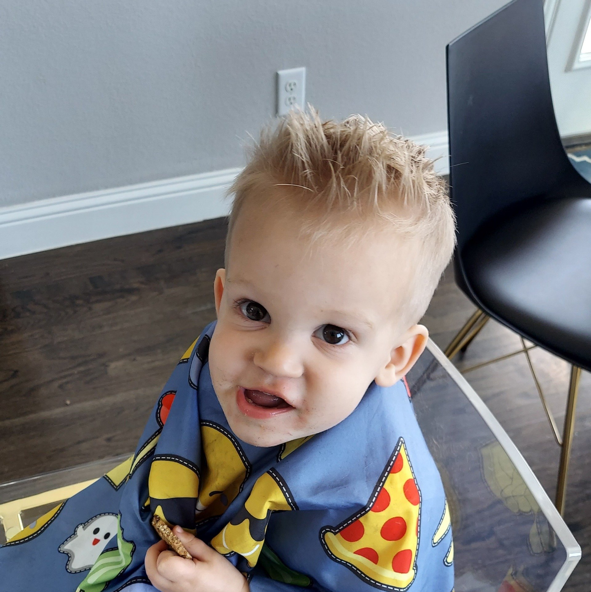 A toddler wearing a blue apron with pizza on it