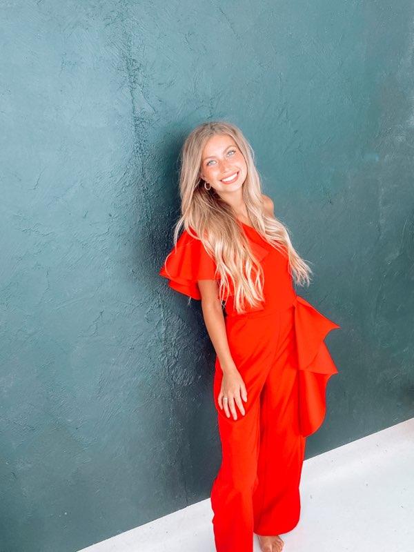 A woman in a red jumpsuit is standing in front of a blue wall.