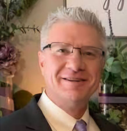 A man wearing glasses and a suit is smiling for the camera