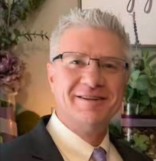 A man wearing glasses and a suit is smiling for the camera