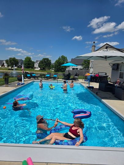 A group of people are swimming in a large swimming pool at Jack Crenshaw's house.