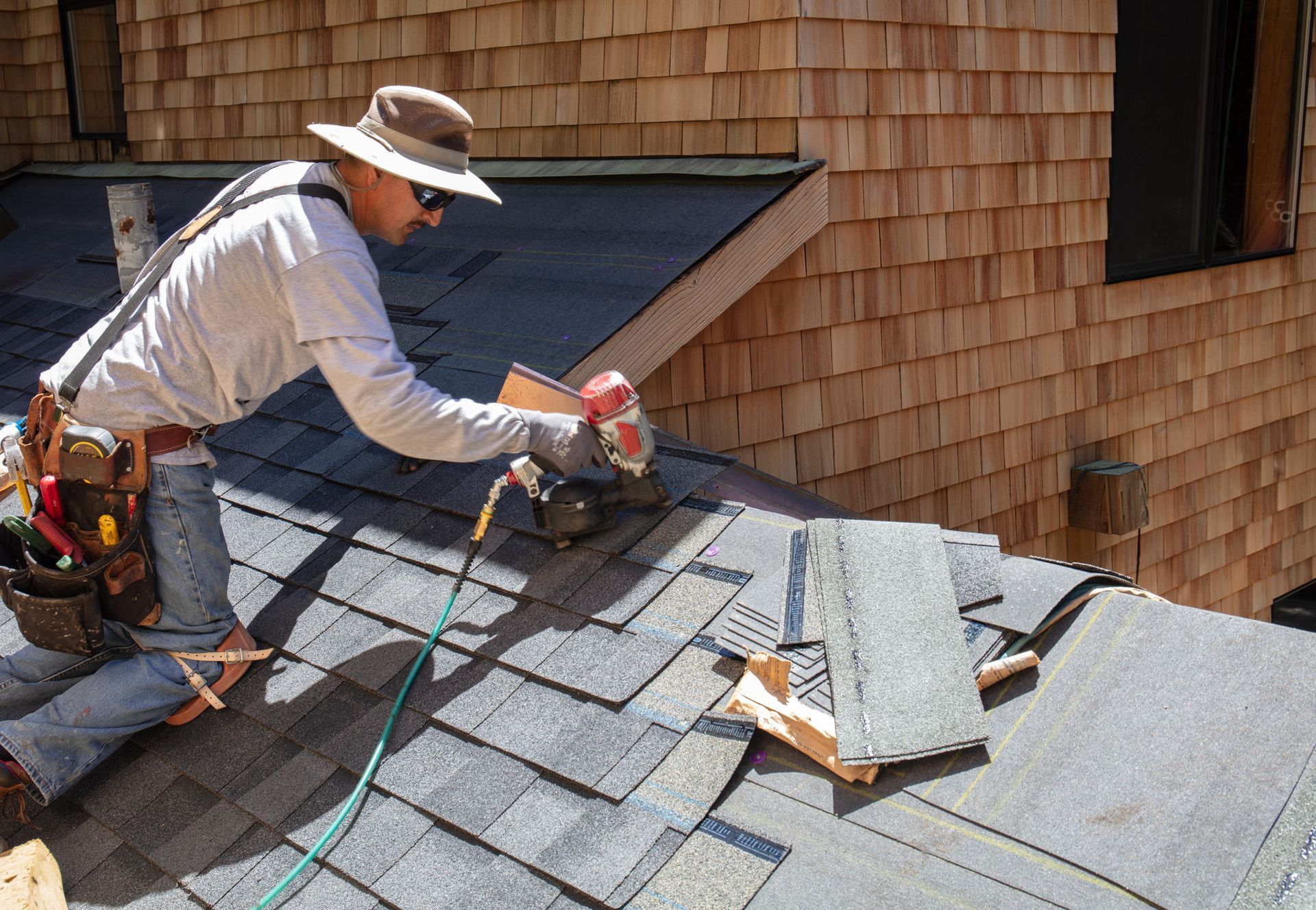 A man installing a new roof with a nail gun and shingles
