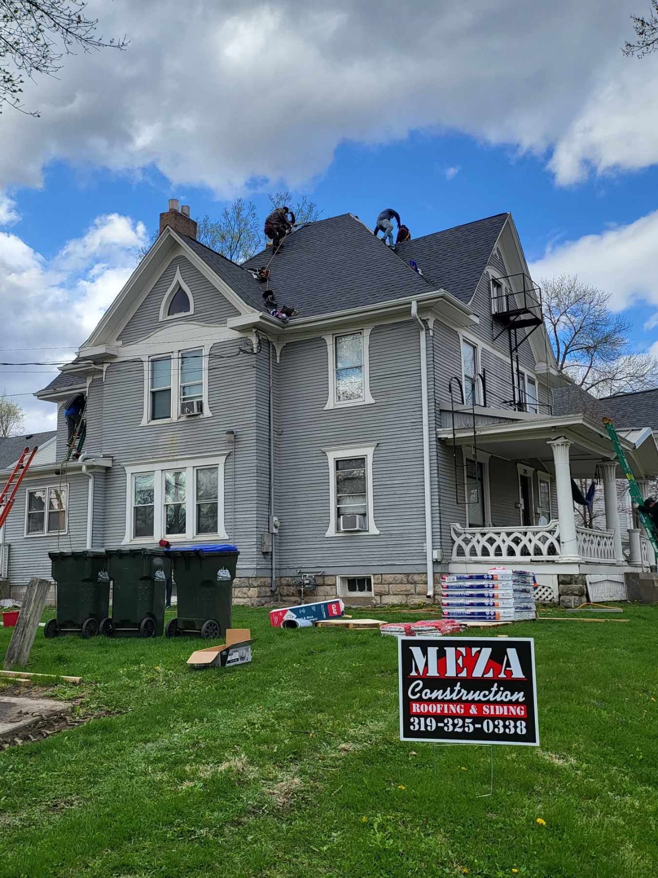 Workers on a gray house roof with new shingles under a cloudy sky. 