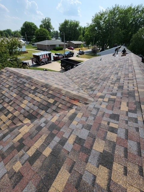 A roof being worked on, with a variety of colored shingles, and workers present.