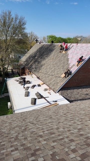 Roofers working on a building with three roof sections. Shingles, materials, and tools are visible. Sunny day.