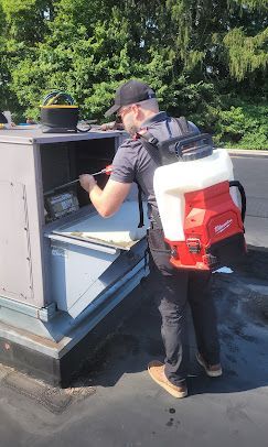 Person standing at an outdoor service counter, reaching into a metal cabinet with a backpack sprayer on