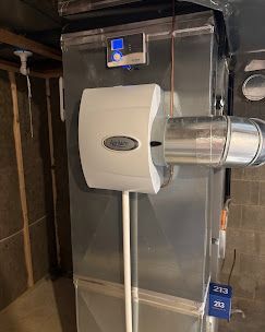 Wall-mounted white ventilation unit with silver ducting in a utility room, with a small digital display above it