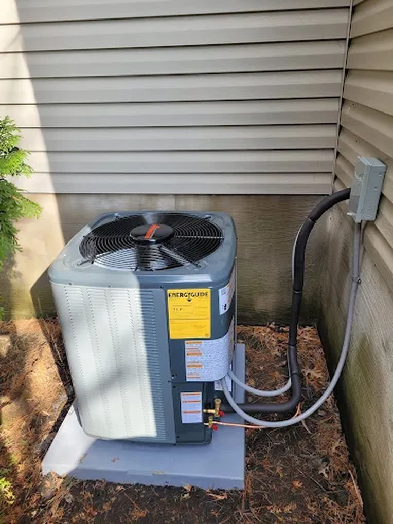 Outdoor air conditioner unit beside a house wall, with hoses and electrical conduit attached