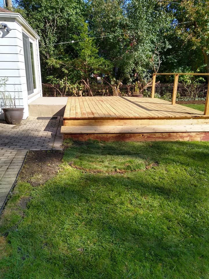 A wooden deck is sitting on top of a lush green lawn next to a house.