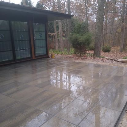 A tiled patio in front of a house in the woods.
