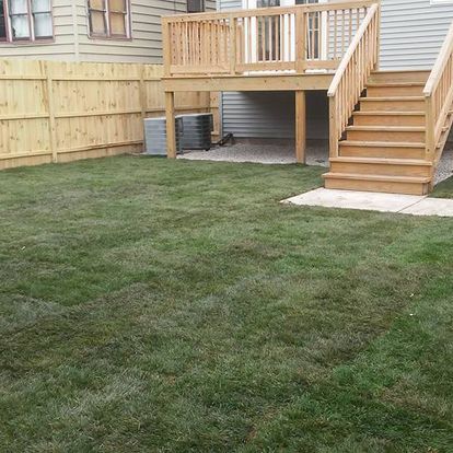 A backyard with a deck and stairs and a wooden fence.
