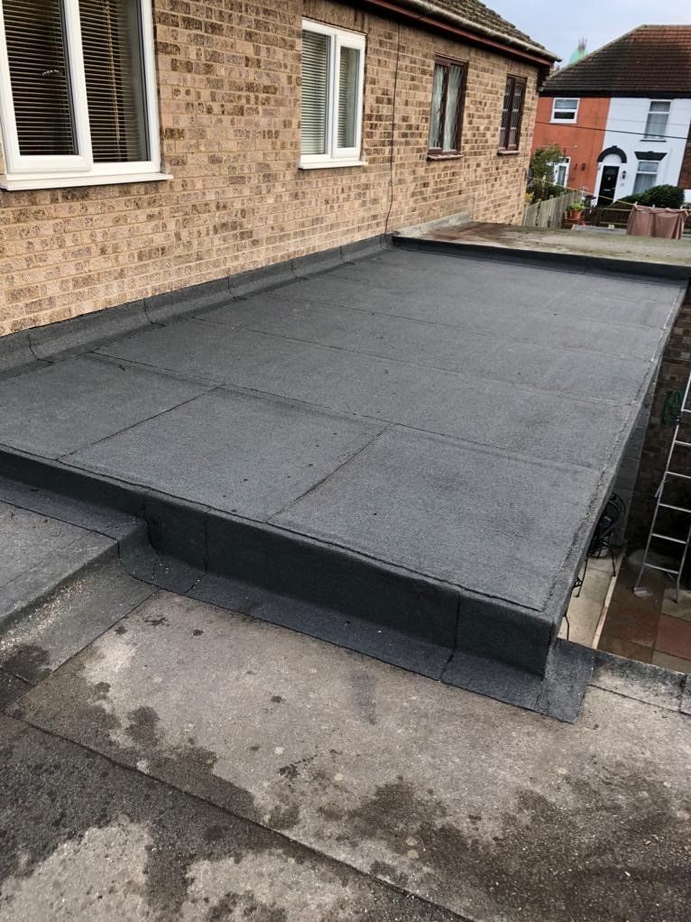 a flat roof is being installed on the side of a brick house .