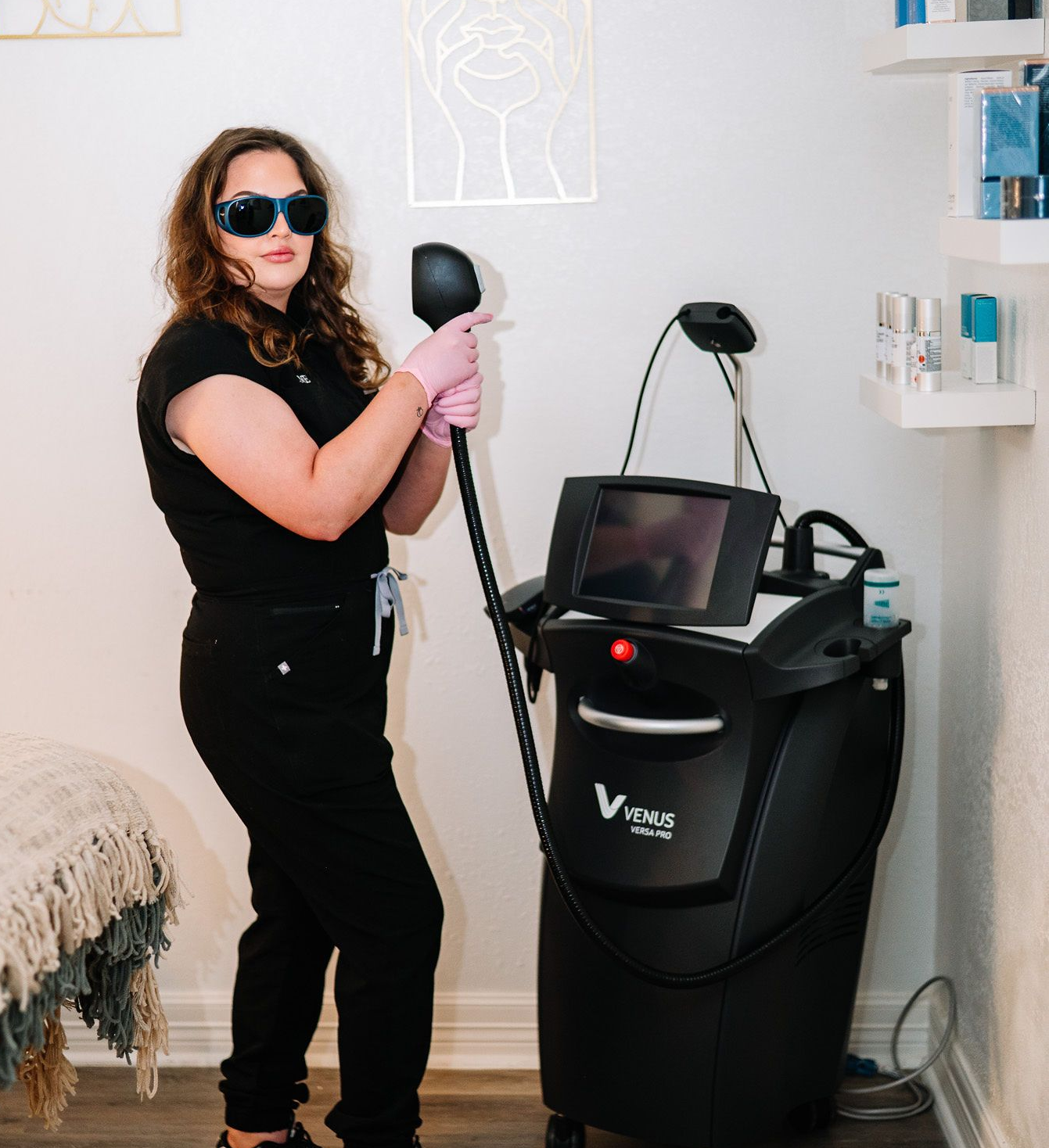 Woman in scrubs holding laser tool, wearing safety glasses, in a spa setting with the Venus Versa device.