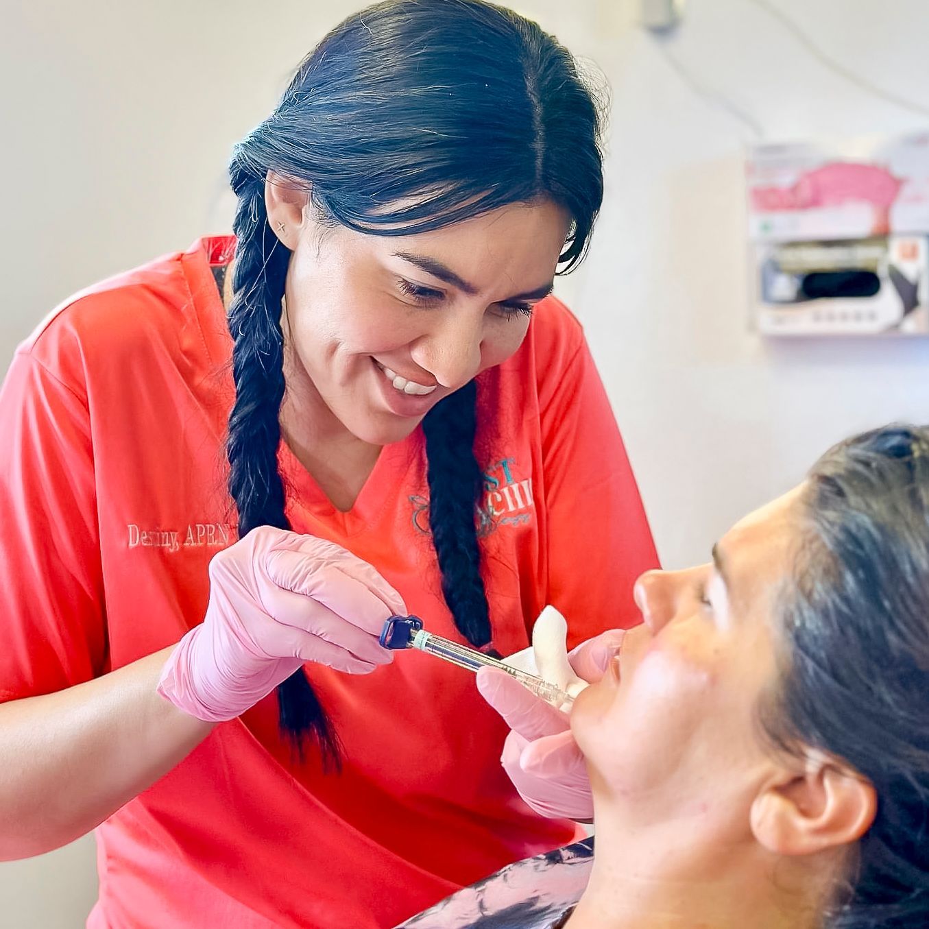 A woman in a red shirt is smiling while holding a syringe in her hand.