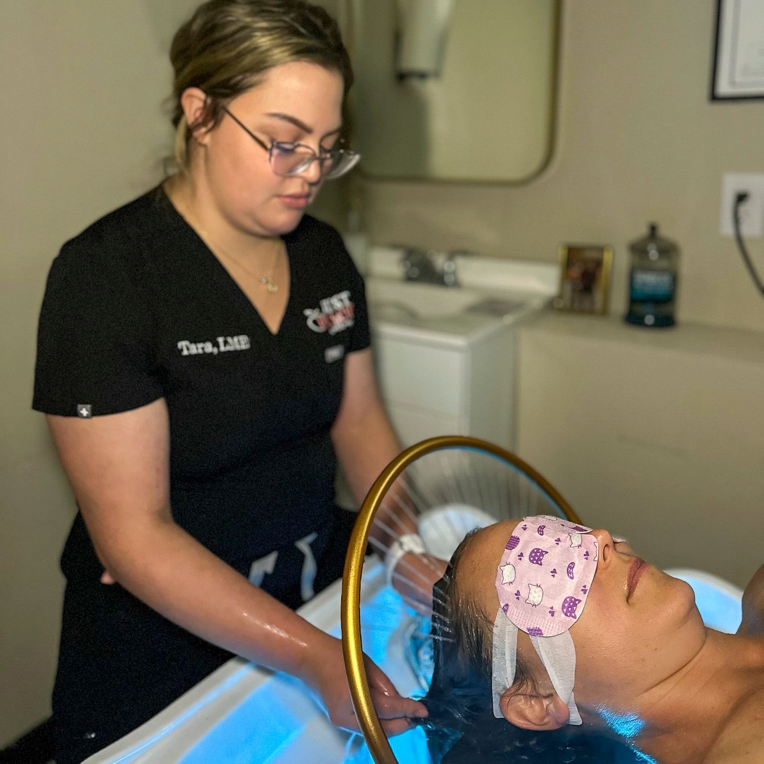 A woman in a black scrub top is washing a woman 's hair