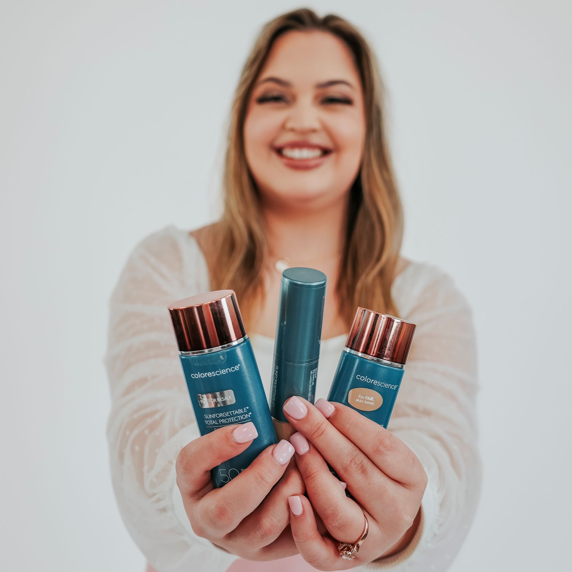 A woman is holding three bottles of cosmetics in her hands.