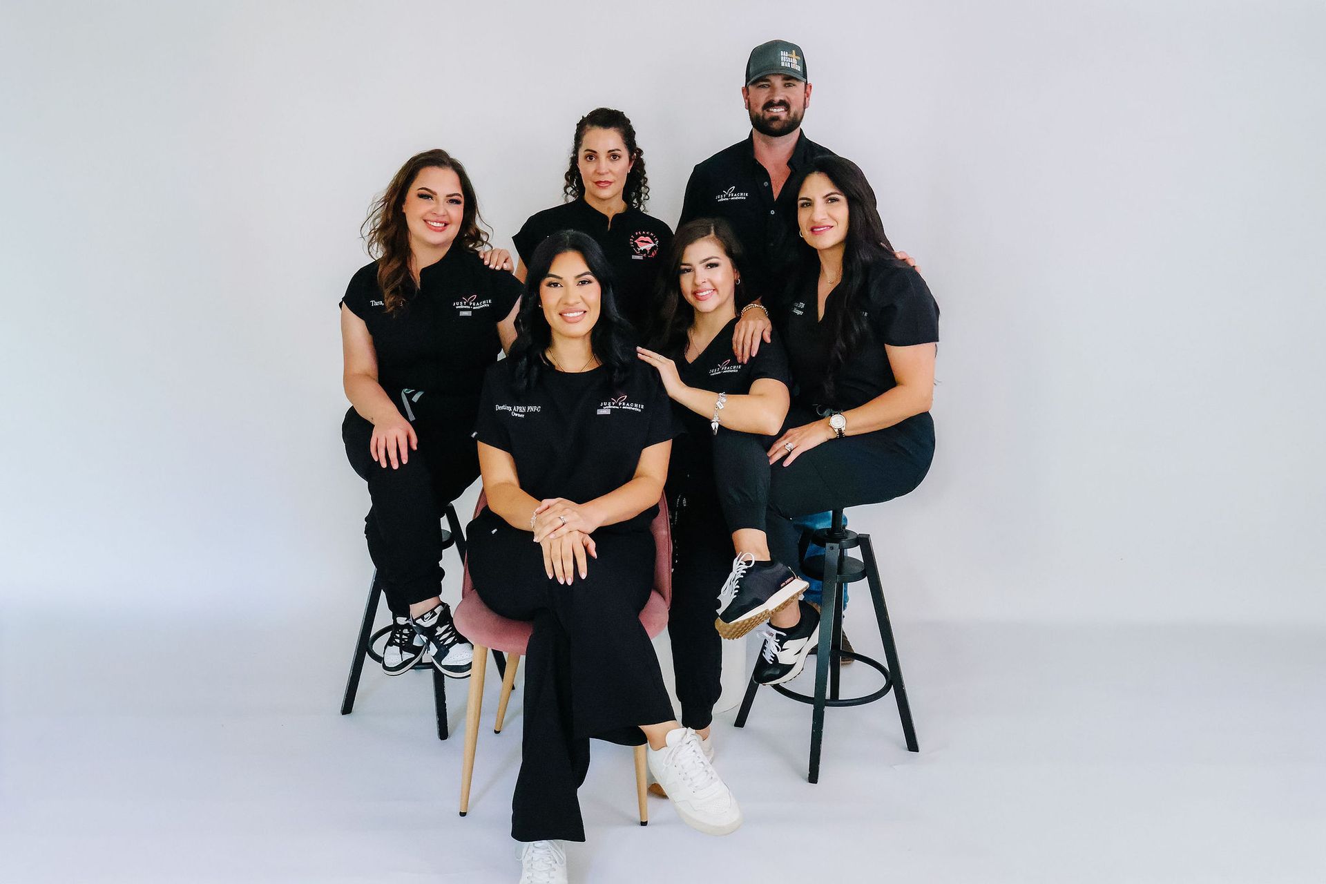 Team of seven people in black scrubs posing in front of a white background.