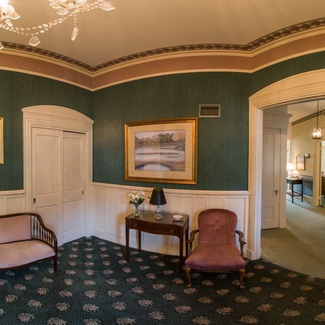 Elegant interior hallway with green patterned carpet, paintings, and antique furniture.
