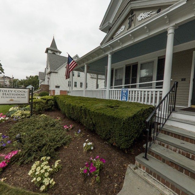 Exterior of a building with a porch and sign; a church steeple is in the background.