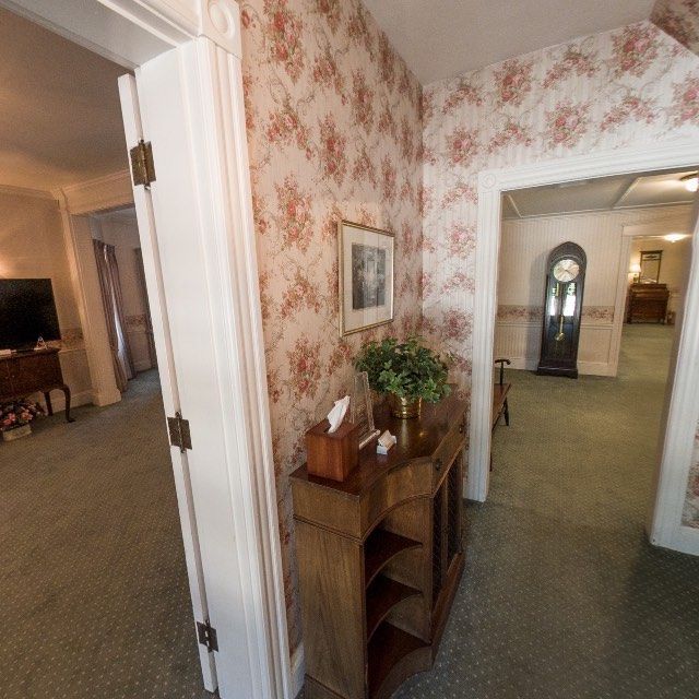 Hallway with floral wallpaper, wooden cabinet with plant and tissue box, and grandfather clock.
