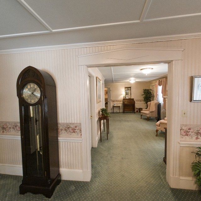 Hallway with green carpet, grandfather clock, and archway to another room.