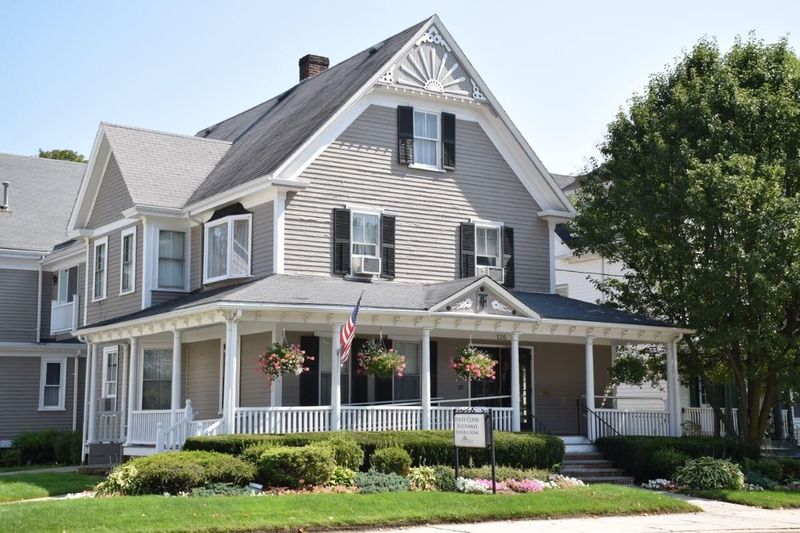 Gray house with white trim, porch, and American flag; landscaping in front.