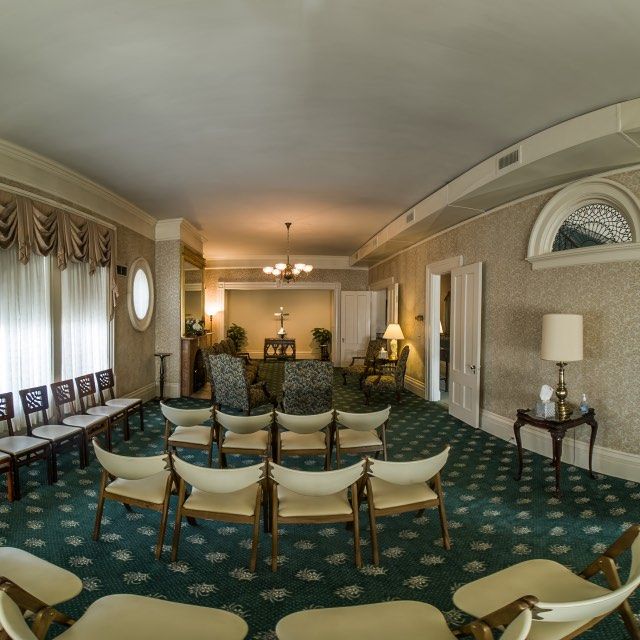 Funeral home chapel, chairs arranged for service, green carpet, soft lighting.