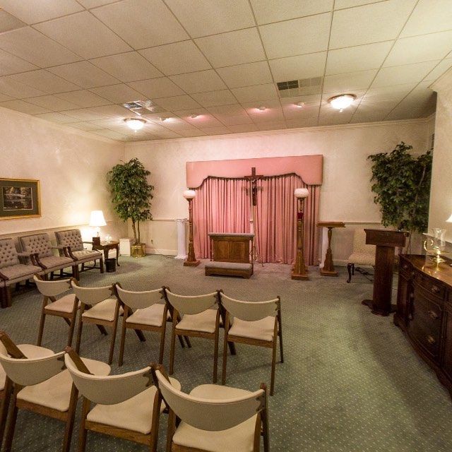 Interior of a funeral home chapel with chairs, a podium, and altar. Pink curtains and beige walls.