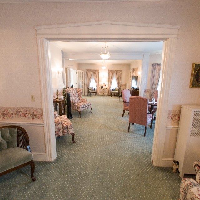 A room with floral patterned chairs and wallpaper, a green carpet, and a large doorway.