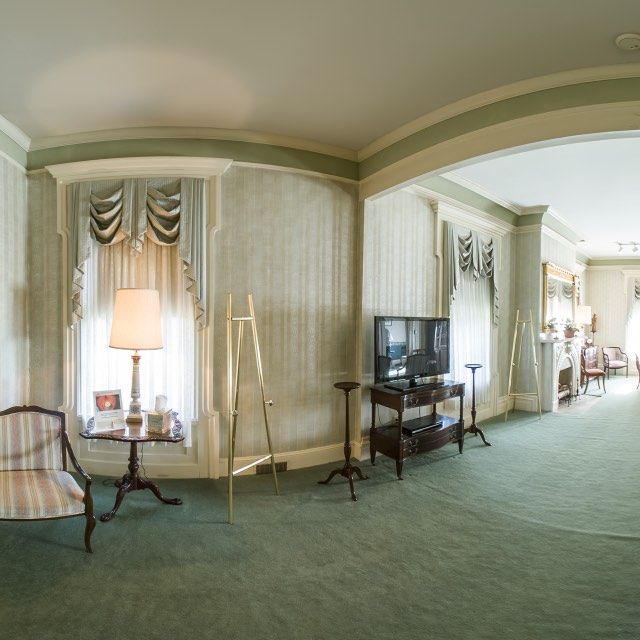 Green-carpeted room with draped windows, a TV, and a vintage chair.