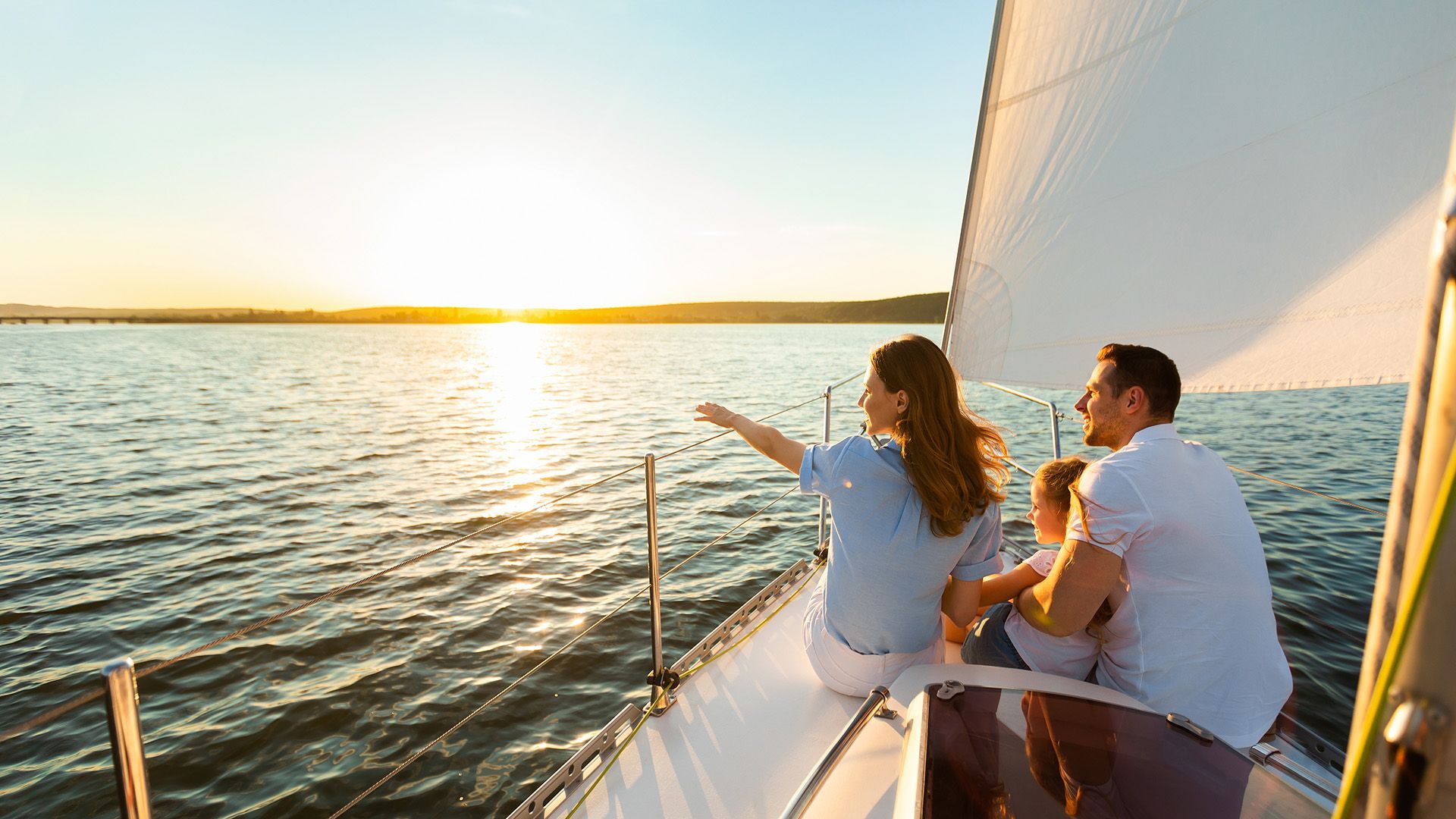 Family on sailboat watches sunset over water.