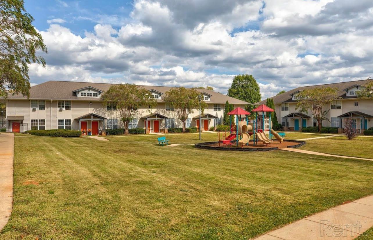 There is a playground in the middle of the grass in front of a row of houses.