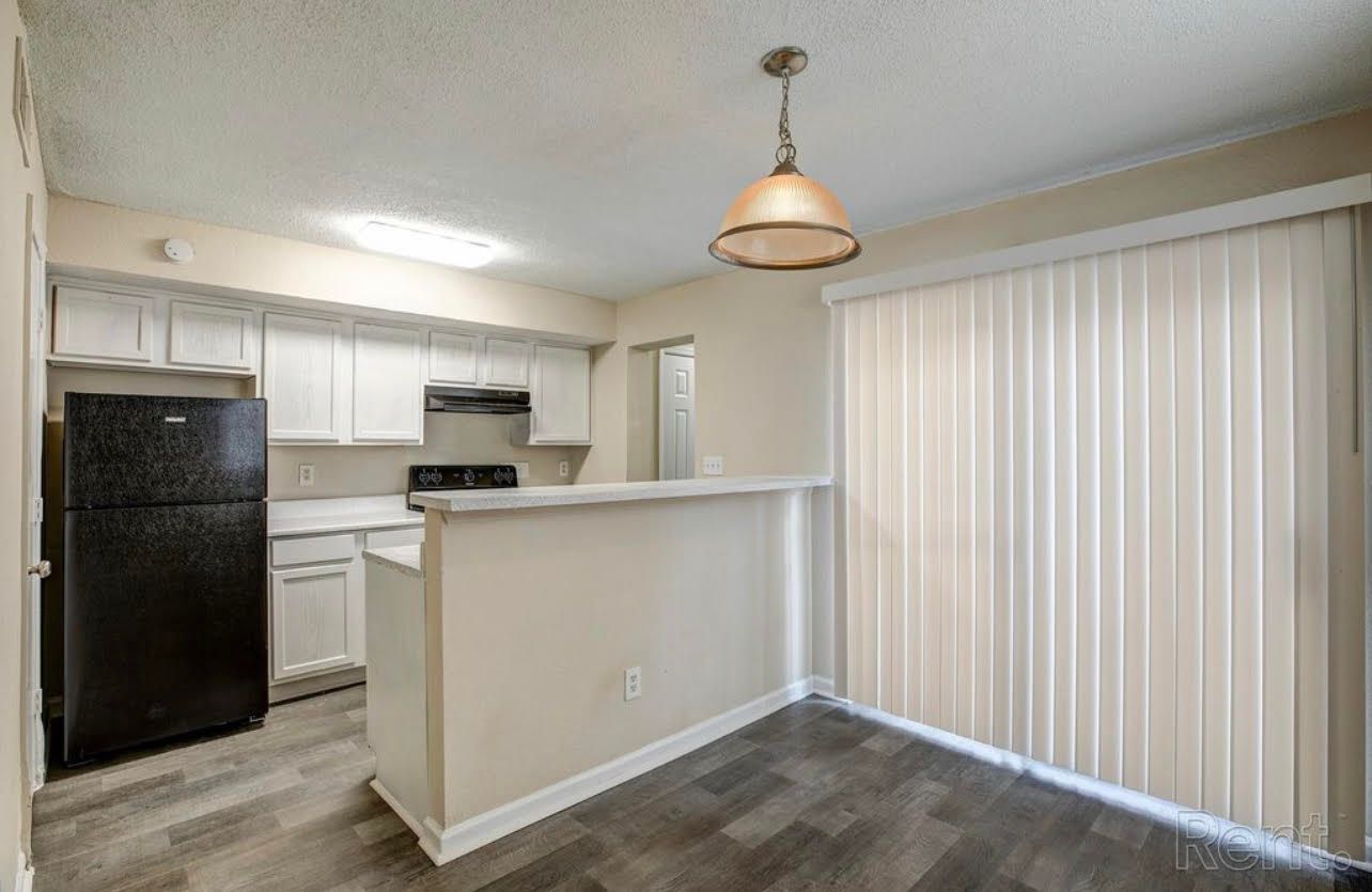 A kitchen with a black refrigerator , white cabinets , and hardwood floors.