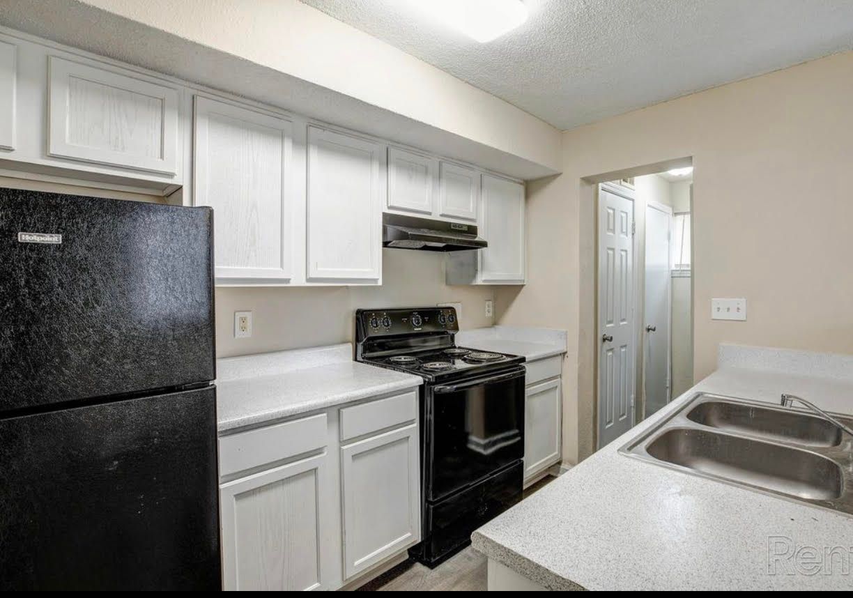 A kitchen with white cabinets , a black refrigerator , a stove , and a sink.