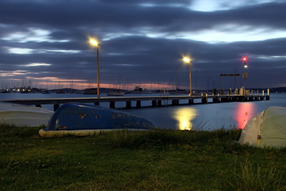 A Boat Is Sitting on The Grass Near a Dock at Night — Custom Cabinetry & Kitchen Renovations in Port Macquarie, NSW