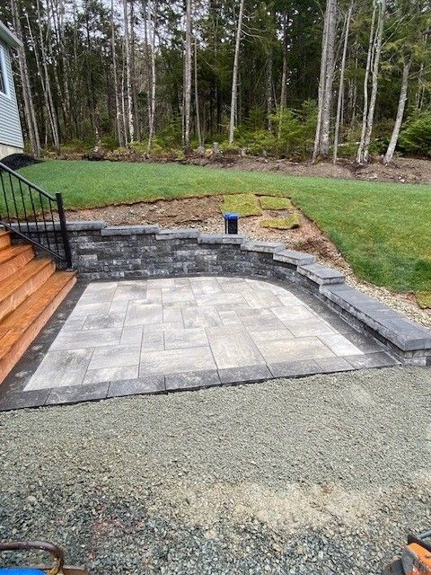 Stone patio with retaining walls, wooden stairs, and grassy area.