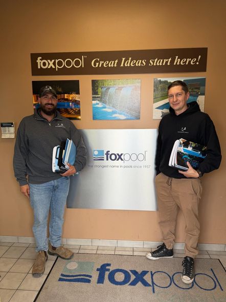 Two men holding items stand in front of a 