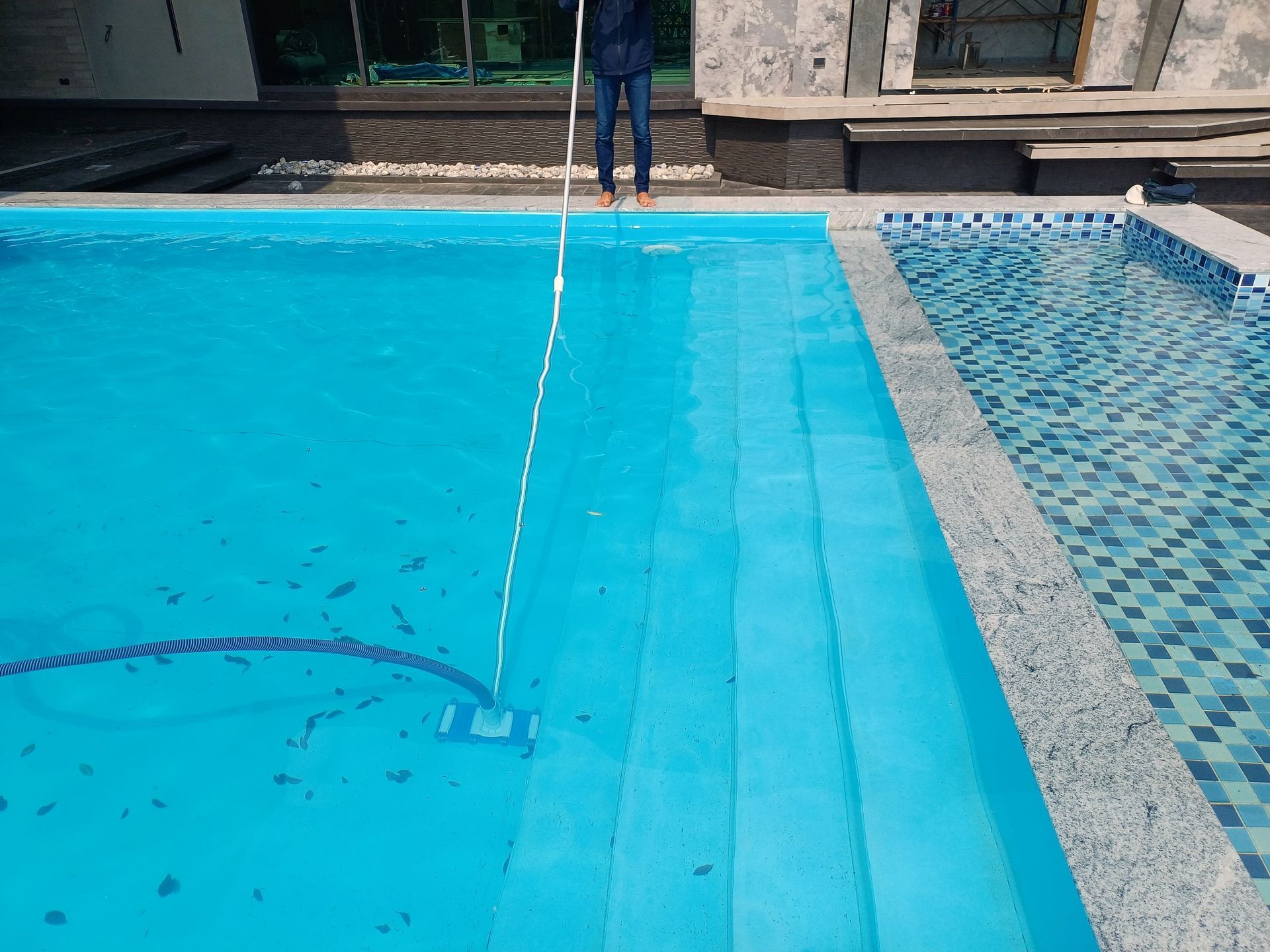 Person vacuuming a blue swimming pool with steps, exterior.
