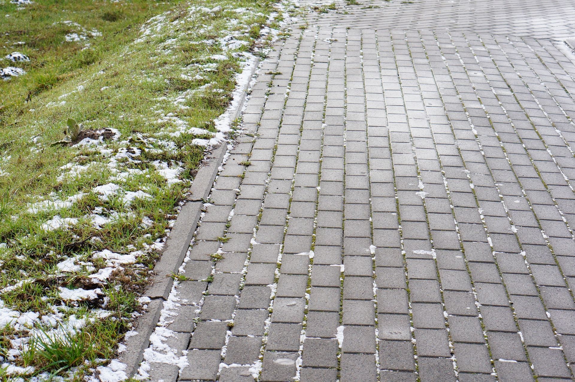Cobblestone path next to grassy embankment, with patches of snow.