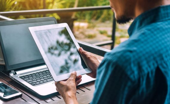 a man is holding a tablet in front of a laptop .