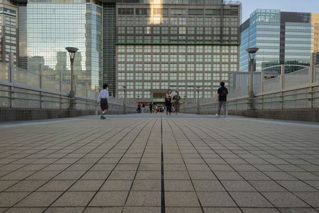 Pedestrian bridge in a city, people walking. Buildings in background.