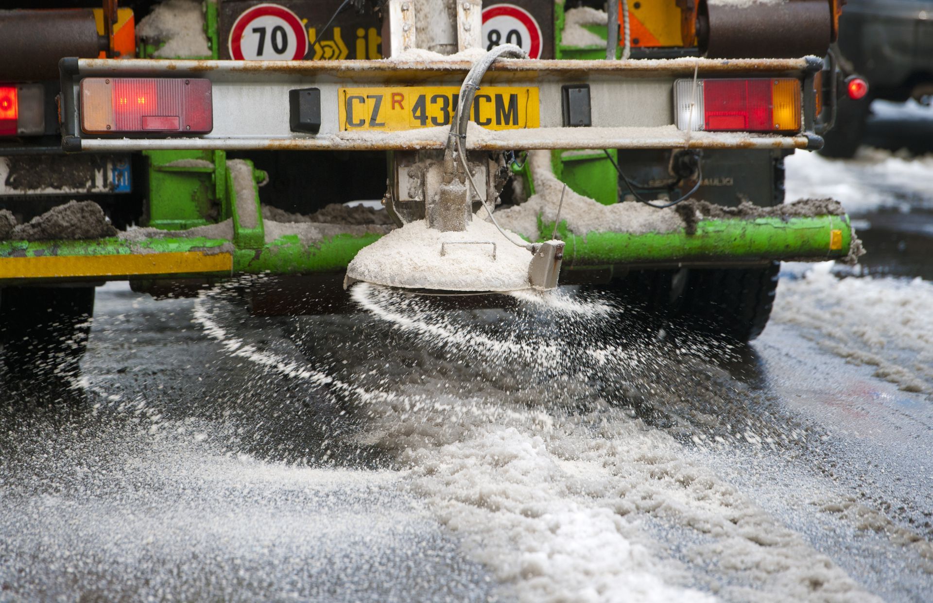 a green and white truck is spreading salt on the road .