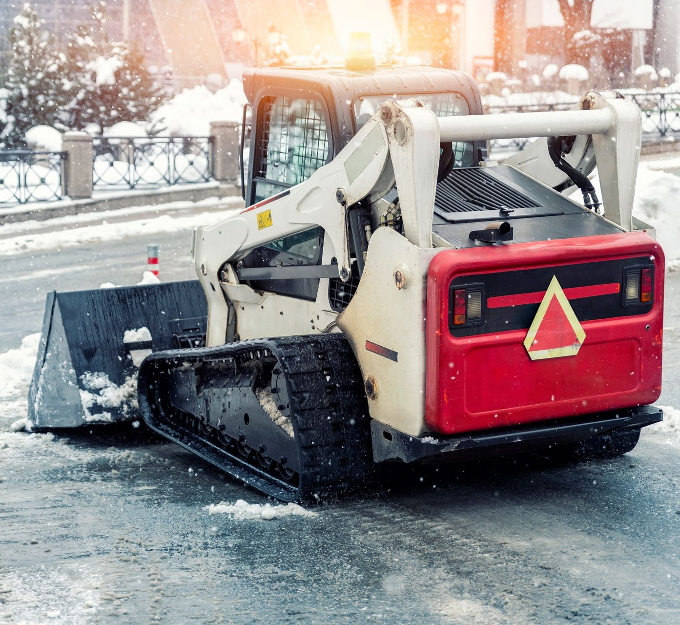 A tracked snowplow with a plow blade clearing snow from a slick road.