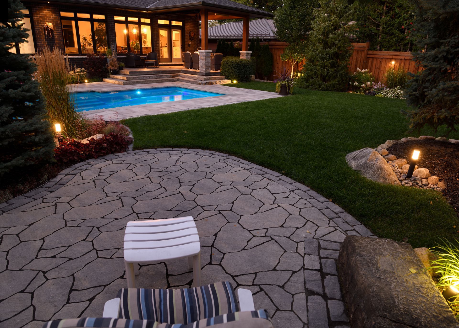 A patio with a chair and ottoman in front of a house with a pool