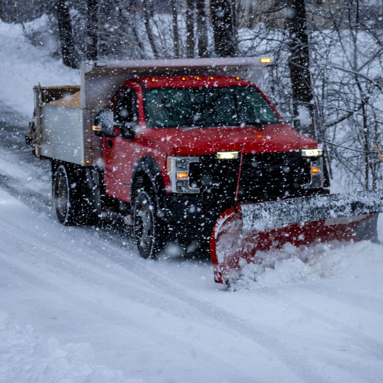 a red truck is plowing snow on a snowy road