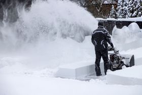 a man is using a snow blower to clear snow from a sidewalk .